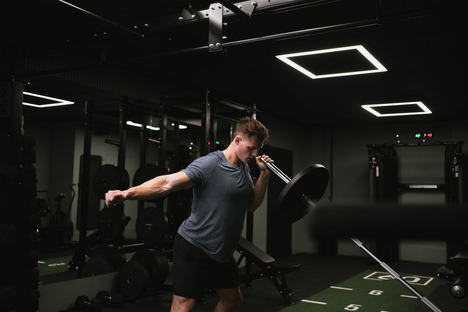 An athlete performs an overhead kettlebell swing exercise in a dimly lit gym setting.