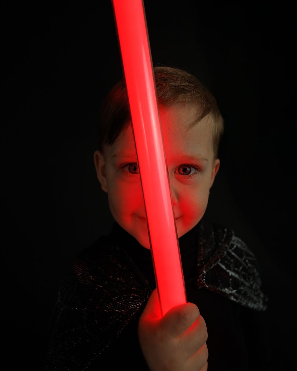 A dark photo illuminated by a glowing red lightsaber casting an eerie crimson glow in the shadows.