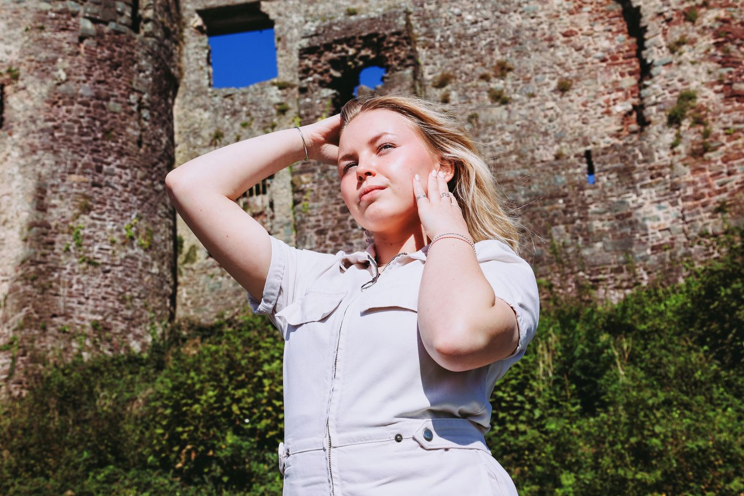 Lifestyle portrait of person in light outfit posing against rustic brick wall with blue window.