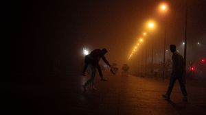 Orange street lights illuminate figures playing soccer in the dark.