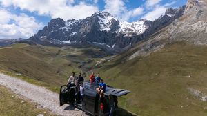 Panoramic mountain landscape with snow-capped peaks and green valleys under blue skies.
