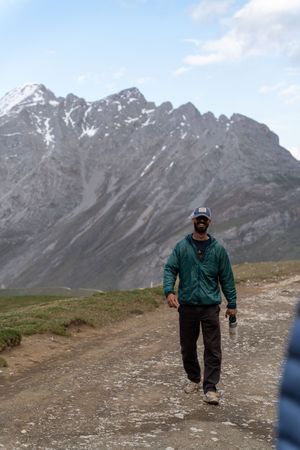 Hiker walking along a mountain trail with snow-capped peaks in the rugged alpine background.