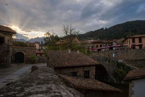 Rural mountain village with traditional stone buildings and dramatic sky at sunset.