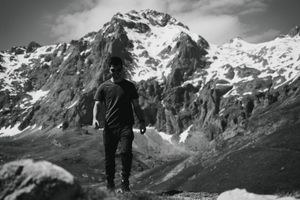 Black and white mountain landscape with hikers silhouetted against snowy peaks.