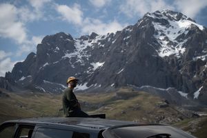 Mountain vista with rocky peaks and snow patches under blue skies and white clouds.