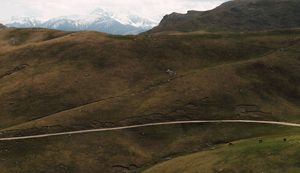 Rolling mountain landscape with winding paths and distant snow-capped peaks.