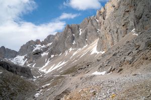 Steep rocky mountain faces with patches of snow against a bright blue sky.