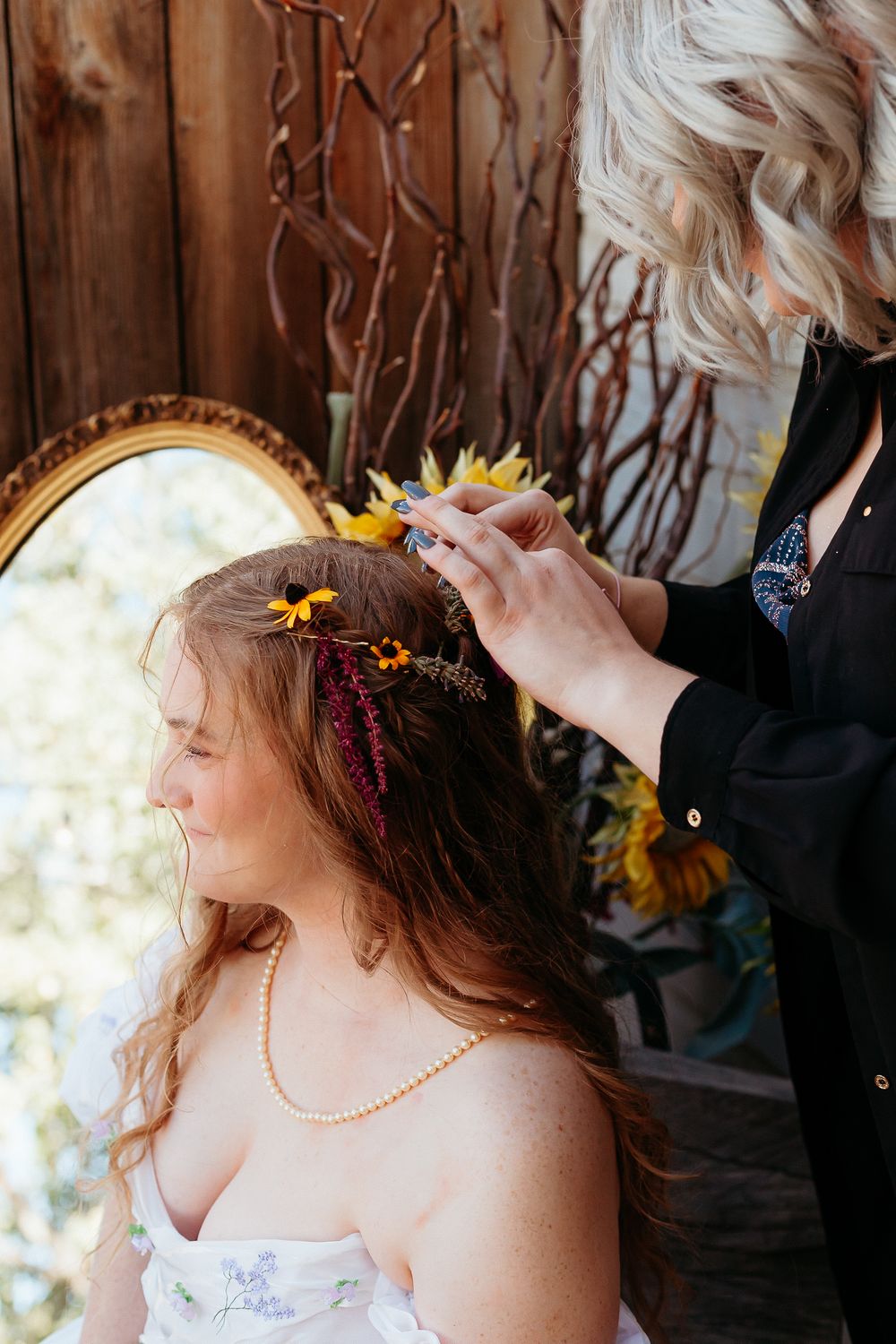 Someone placing a delicate sunflower crown on long wavy hair during a wedding preparation.