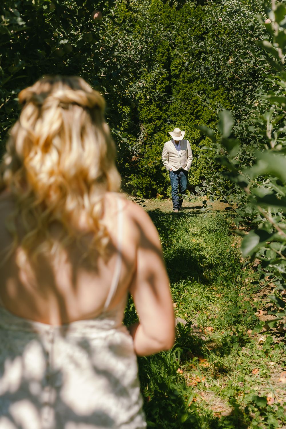 A sunny outdoor garden scene with two people amid lush greenery and dappled sunlight on a garden path.