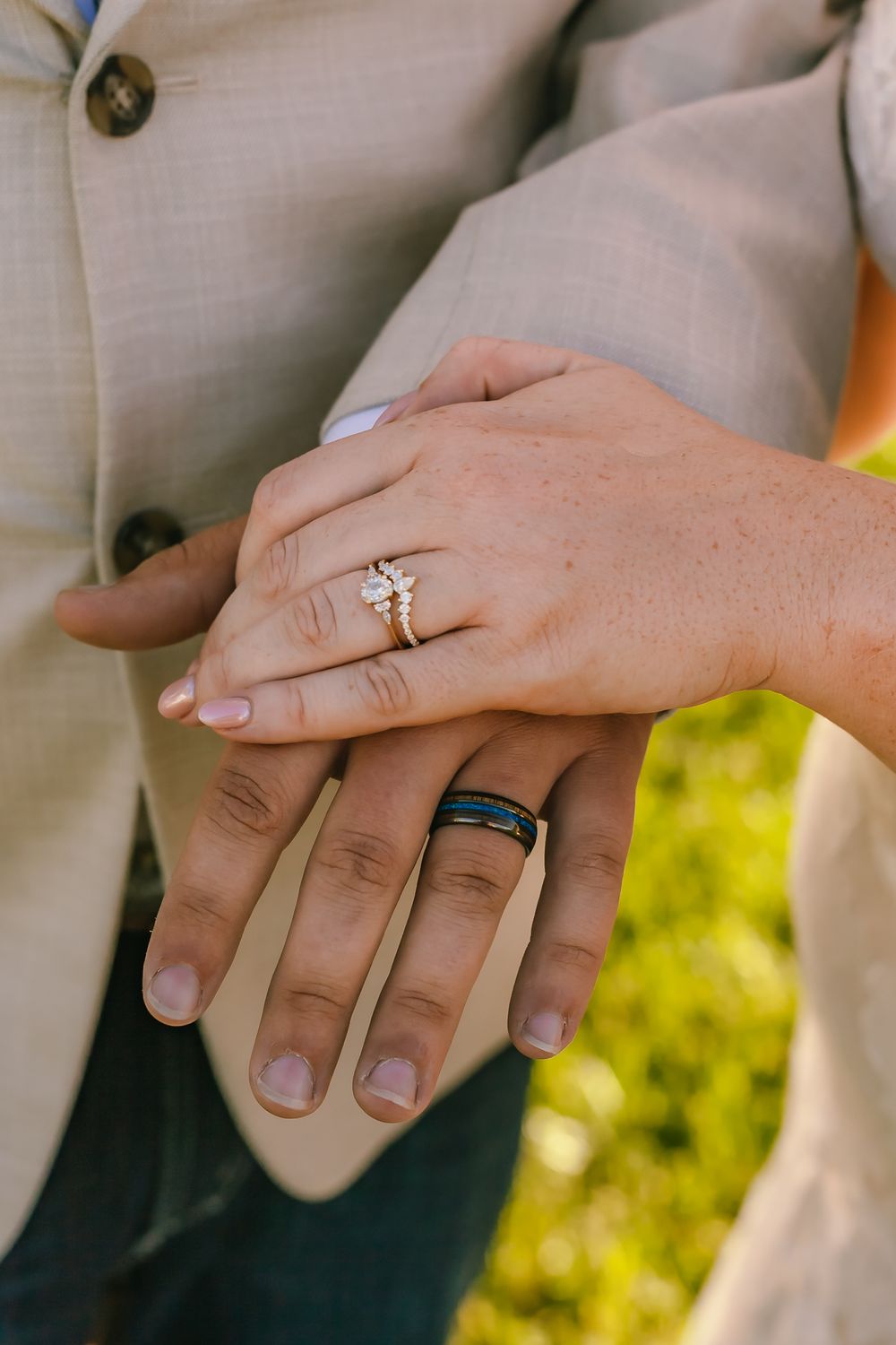 Close-up of hands wearing wedding rings with one silver band and one black band against light colored clothing.