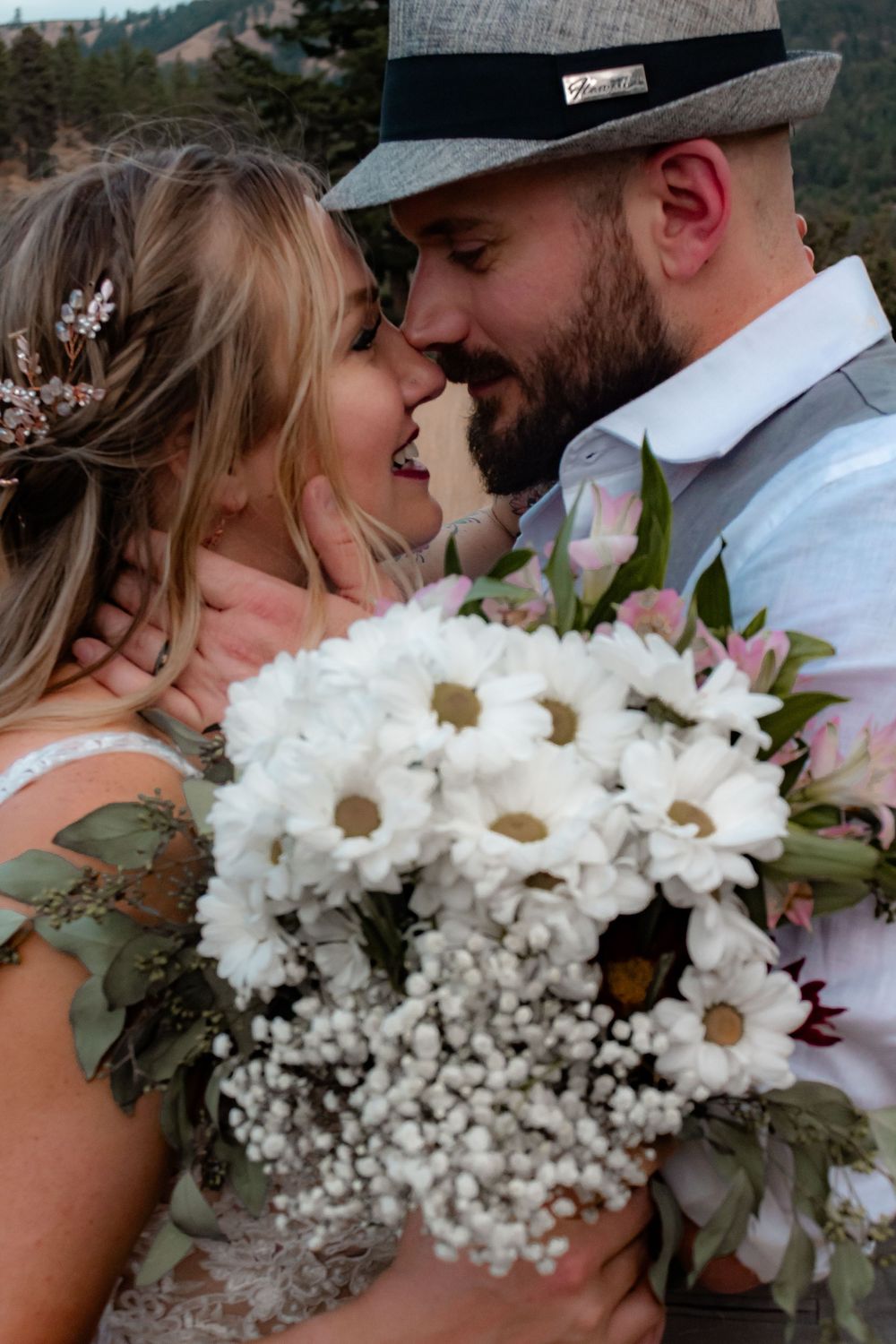 Romantic wedding photo featuring a bride holding white daisies and baby's breath bouquet while sharing an intimate moment outdoors.