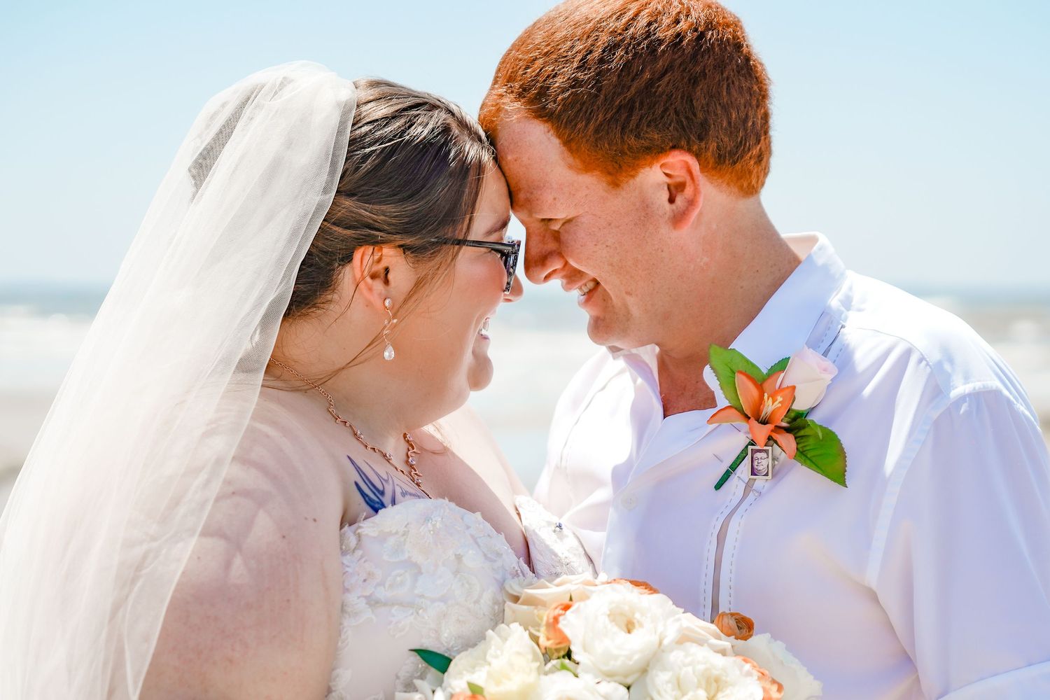 A couple shares an intimate moment on their wedding day at the beach with the bride in white and groom wearing a boutonniere.