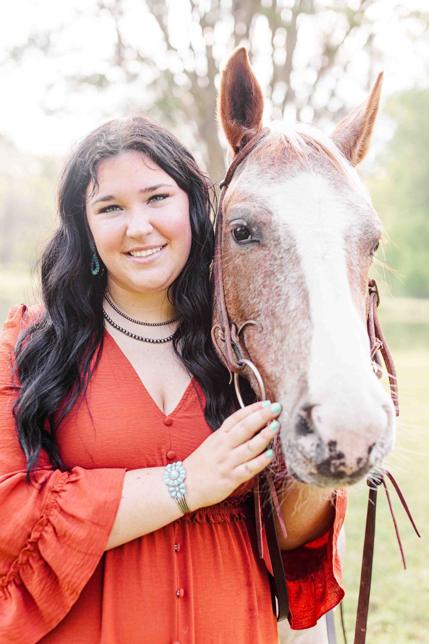 A beautiful paint horse poses with someone wearing a red dress outdoors in soft natural lighting.