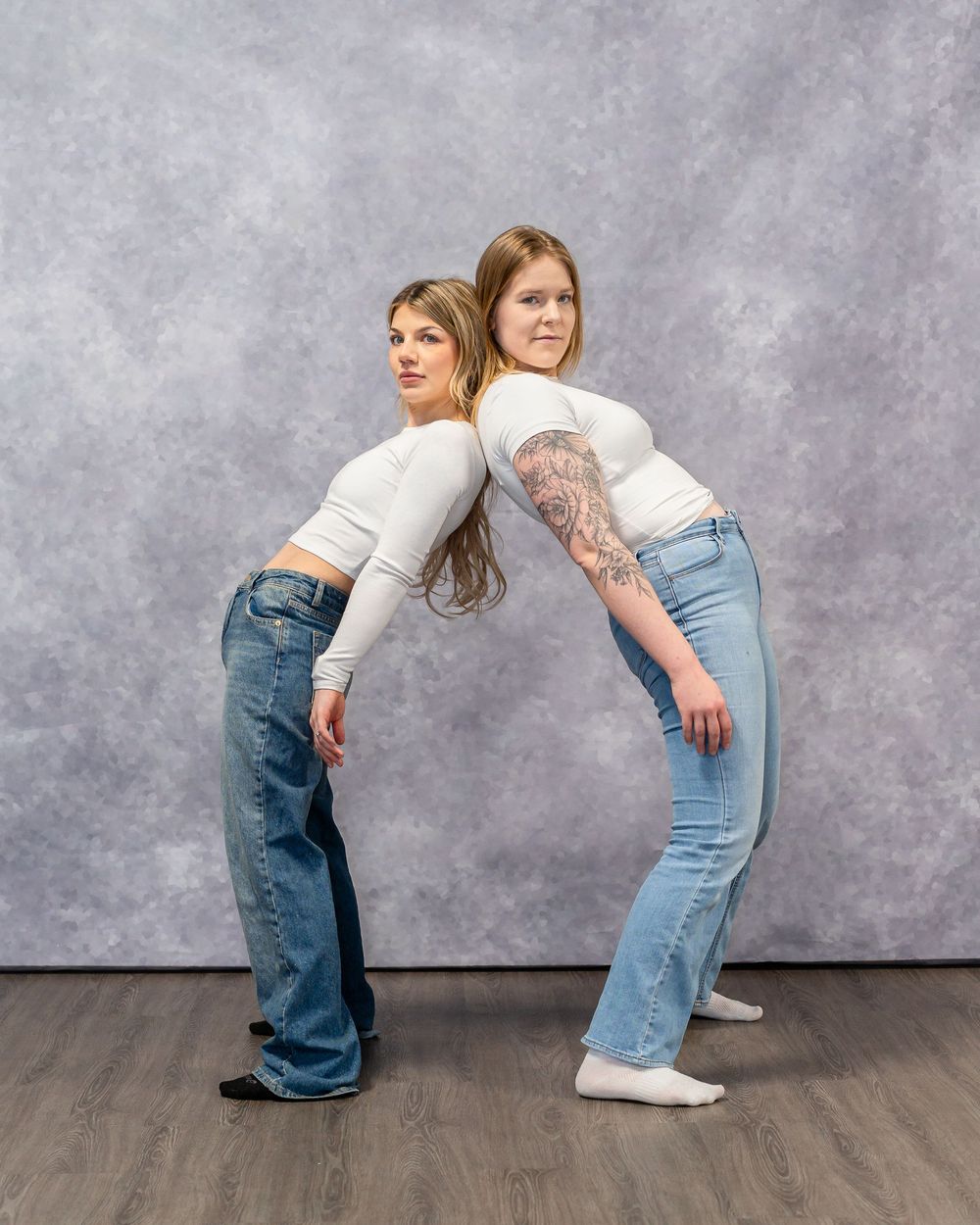 Two models in matching outfits pose back-to-back against studio backdrop.