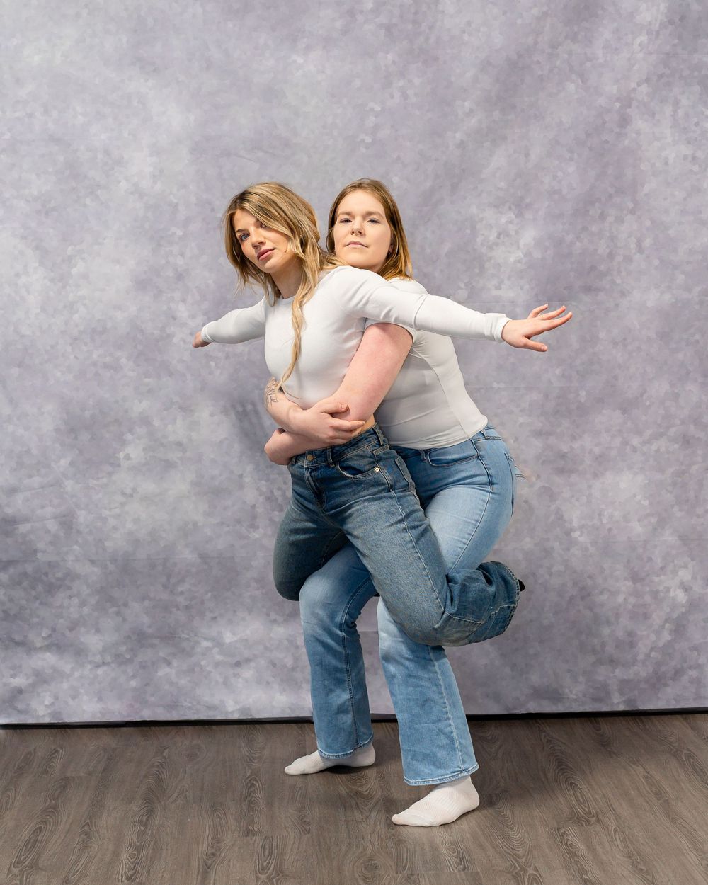 Playful dance pose with two people in matching outfits against gray studio background.