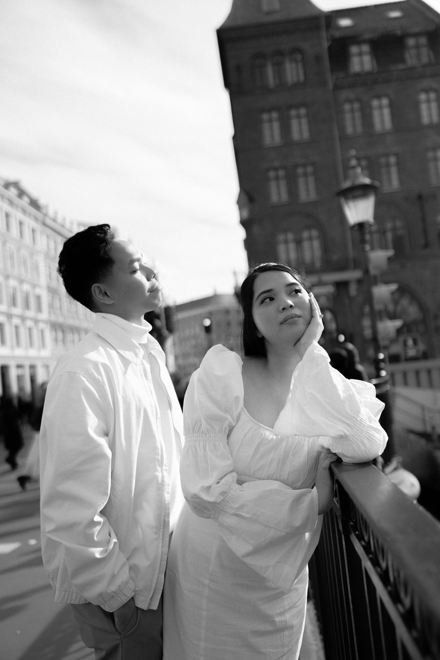A couple in white clothing poses playfully on a city street with historic architecture in the background. Wedding in Copenhagen, Denmark.