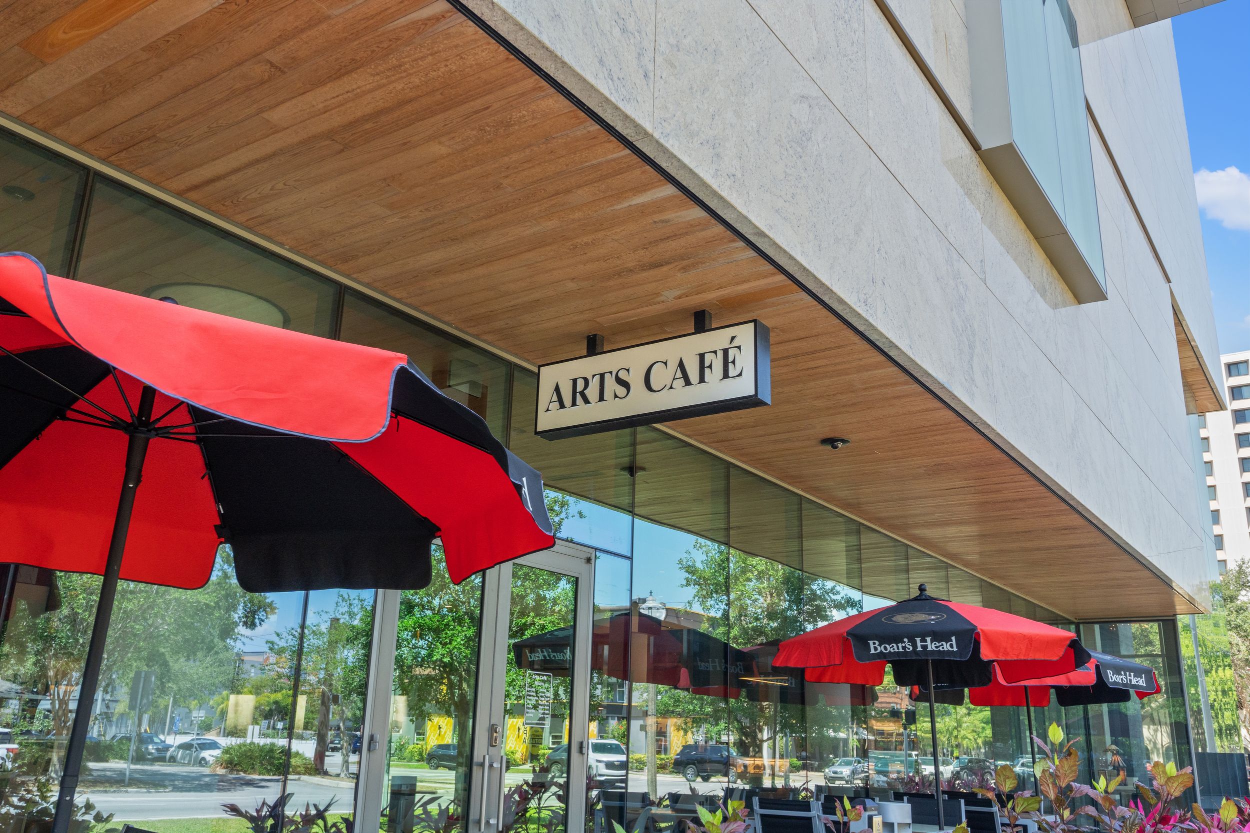 Exterior view of modern arts cafe with red awnings and wooden ceiling overhang.