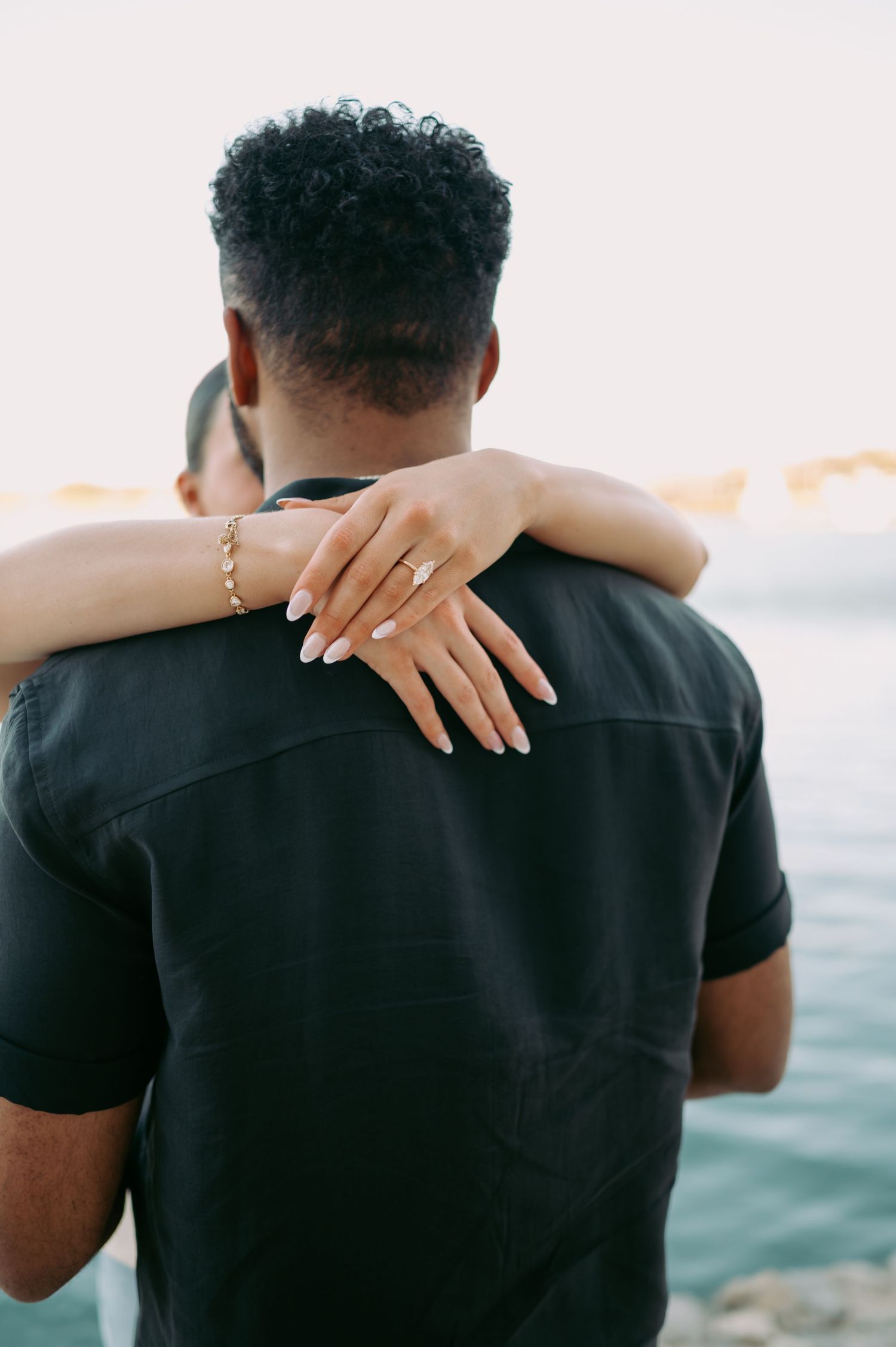 Close up of hands embracing during romantic waterfront engagement photo.