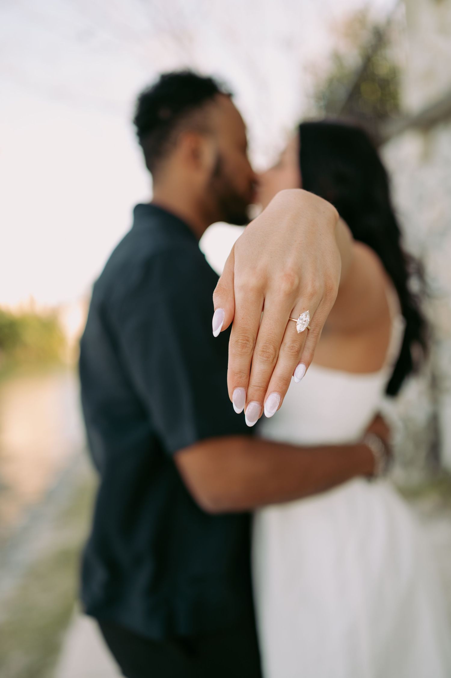 Close up of engagement ring on woman's hand while couple embraces.