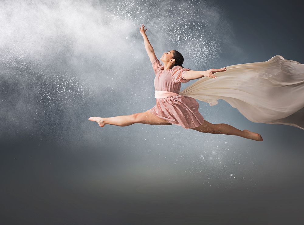 A dancer in pink dress leaps gracefully through a cloud of white powder against a dark dramatic background.