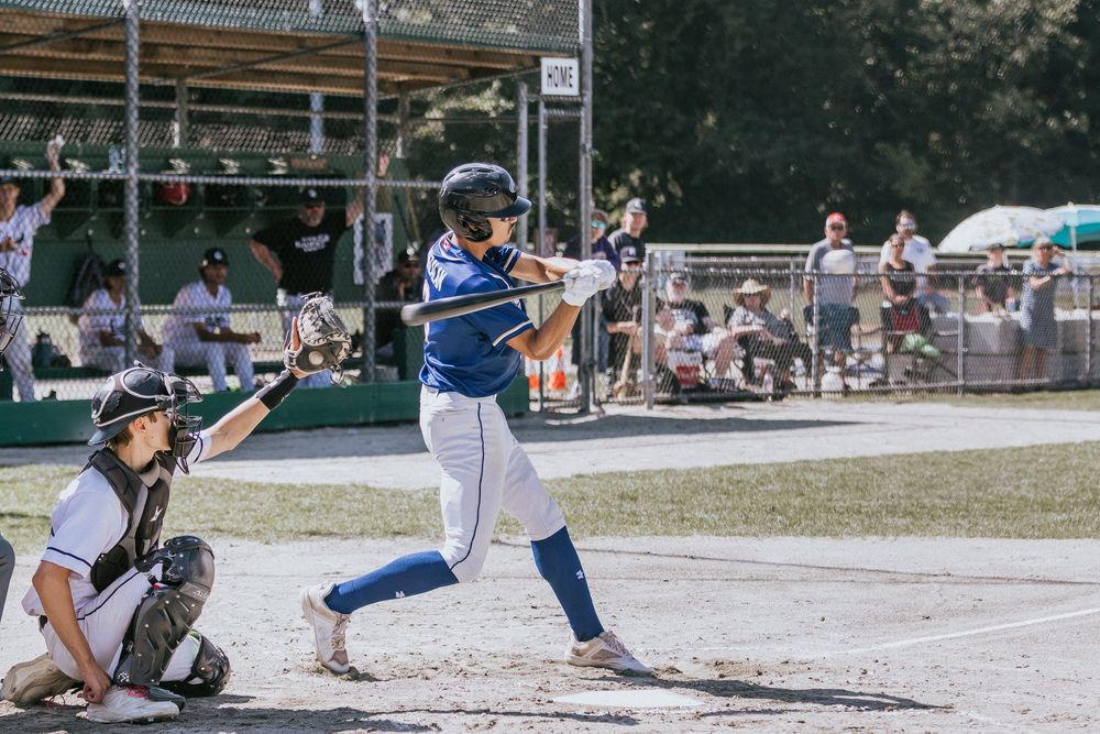 Baseball player in blue uniform swings bat while catcher crouches behind home plate during outdoor game.