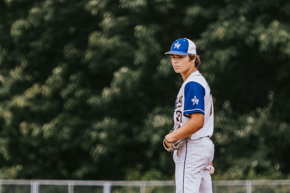 A baseball player in a white and blue uniform stands ready on the pitchers mound during a game.