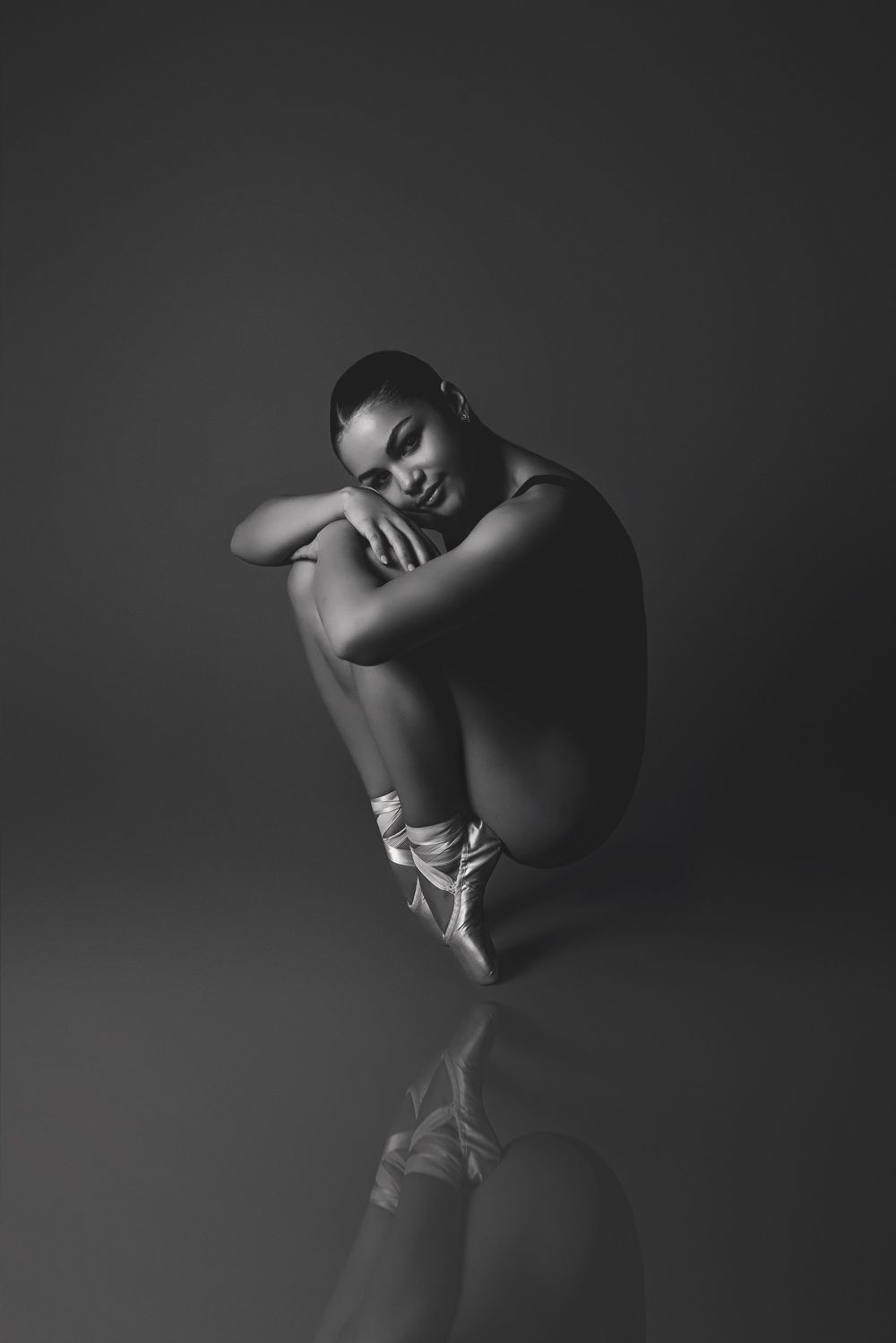 A ballet dancer in pointe shoes poses gracefully in a reflective black and white artistic portrait.
