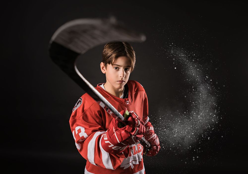 Hockey player in red jersey swings stick with dramatic motion effect against black background.