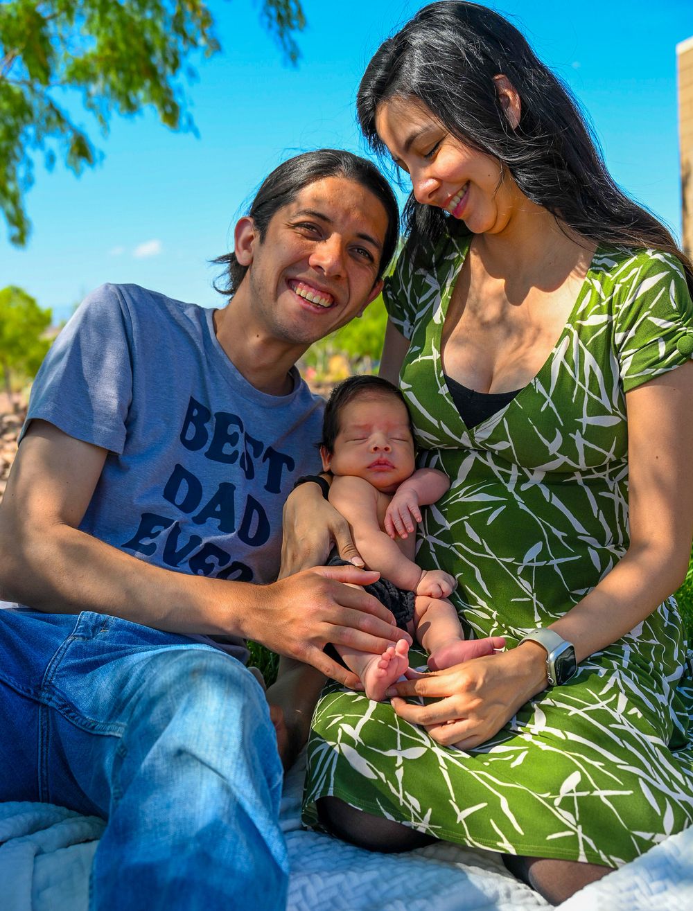 Happy young family with father in Best Dad Ever shirt posing with newborn baby outdoors.