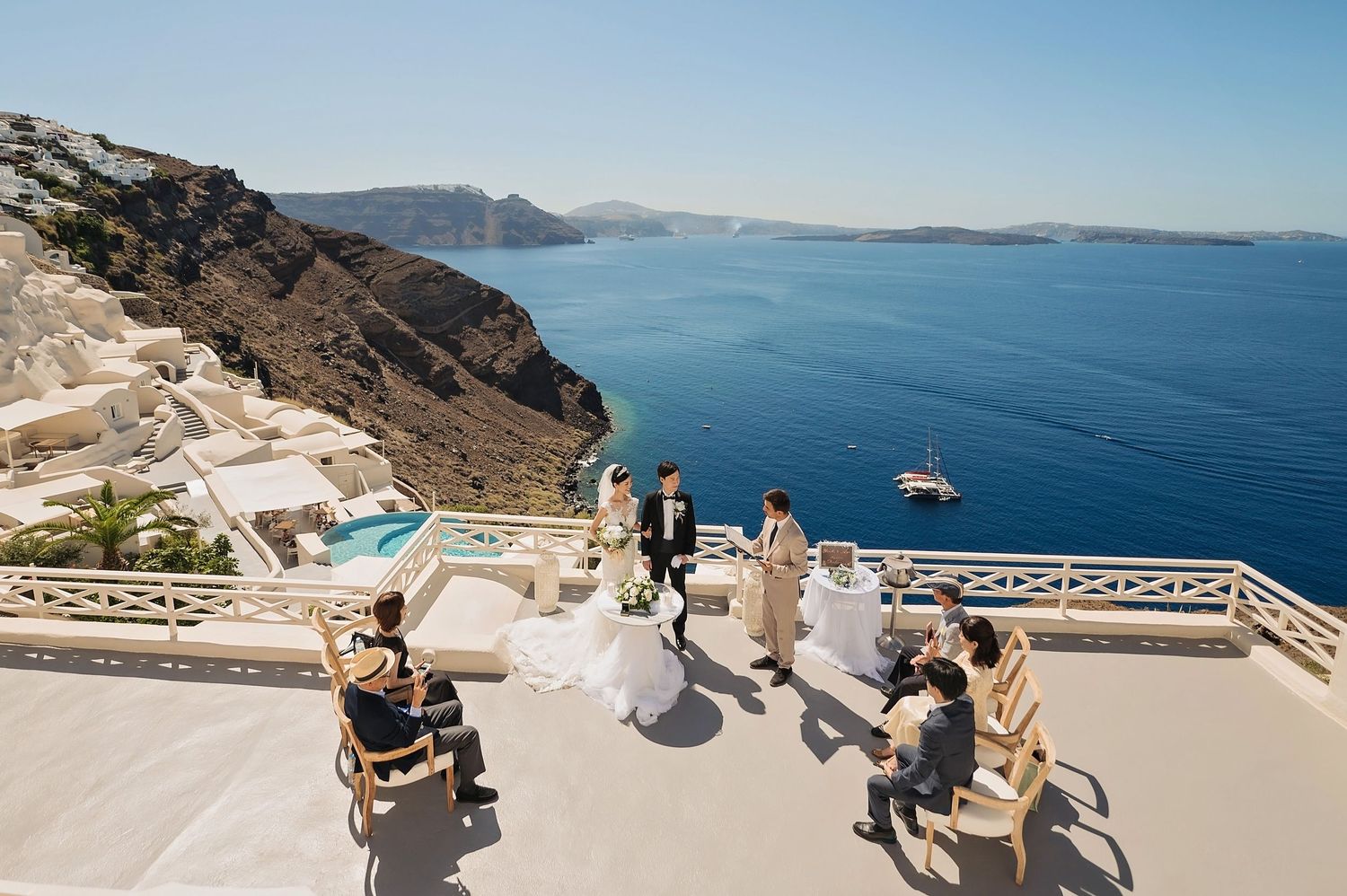Outdoor wedding ceremony with guests seated on a white terrace overlooking the Mediterranean Sea.