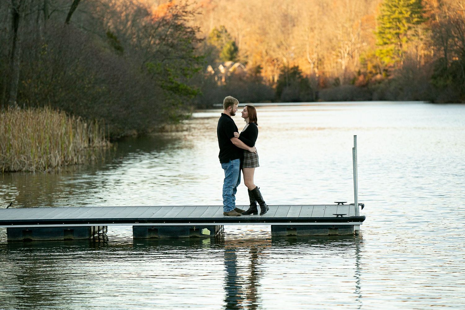 Romantic couple poses on wooden dock by lake during golden hour.