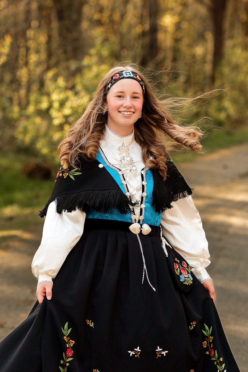 En smilende konfirmant som svinger seg med bunaden i en skog på Ølberg.