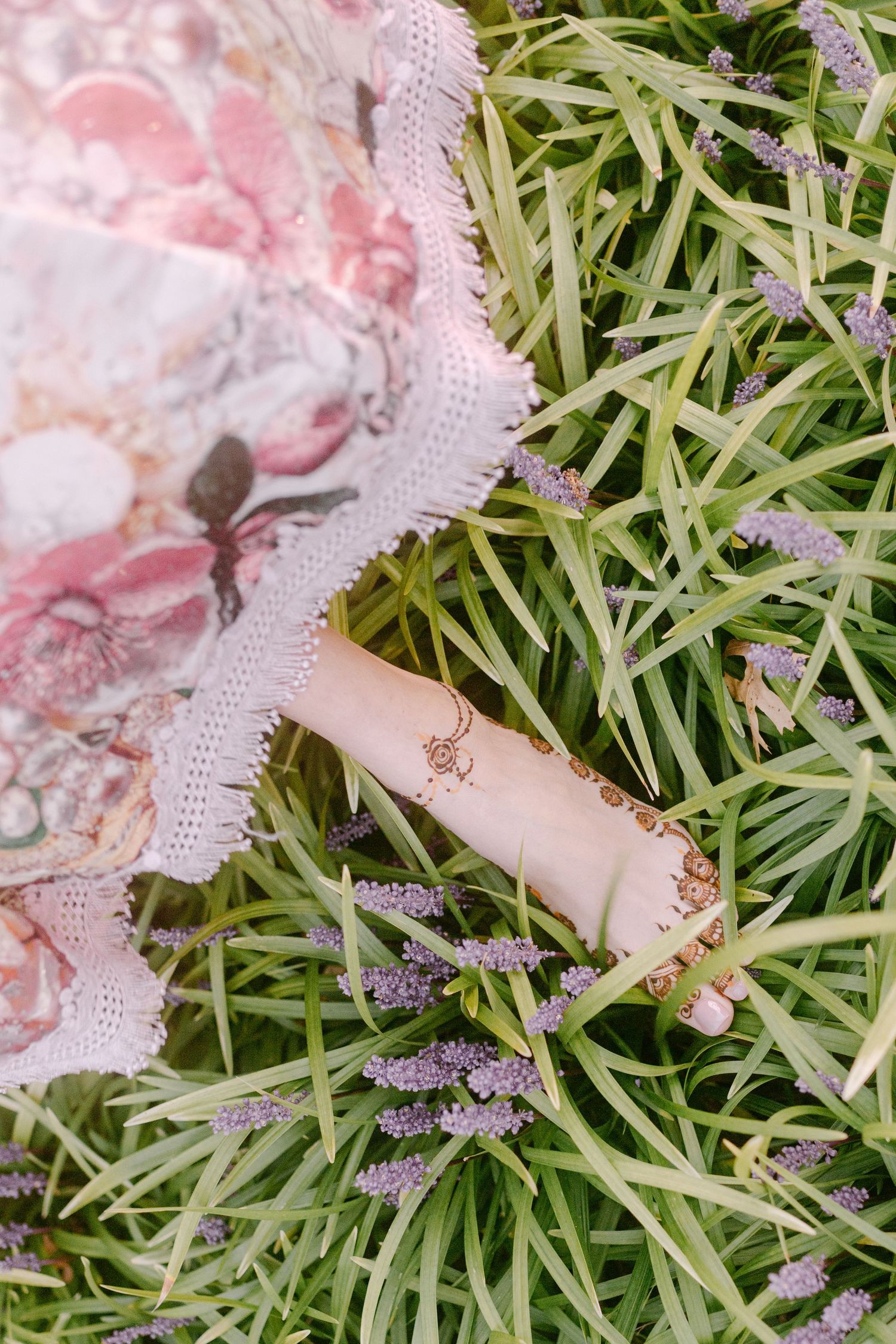 Delicate pink lace fabric and ribbons arranged on fresh green grass with lavender sprigs.