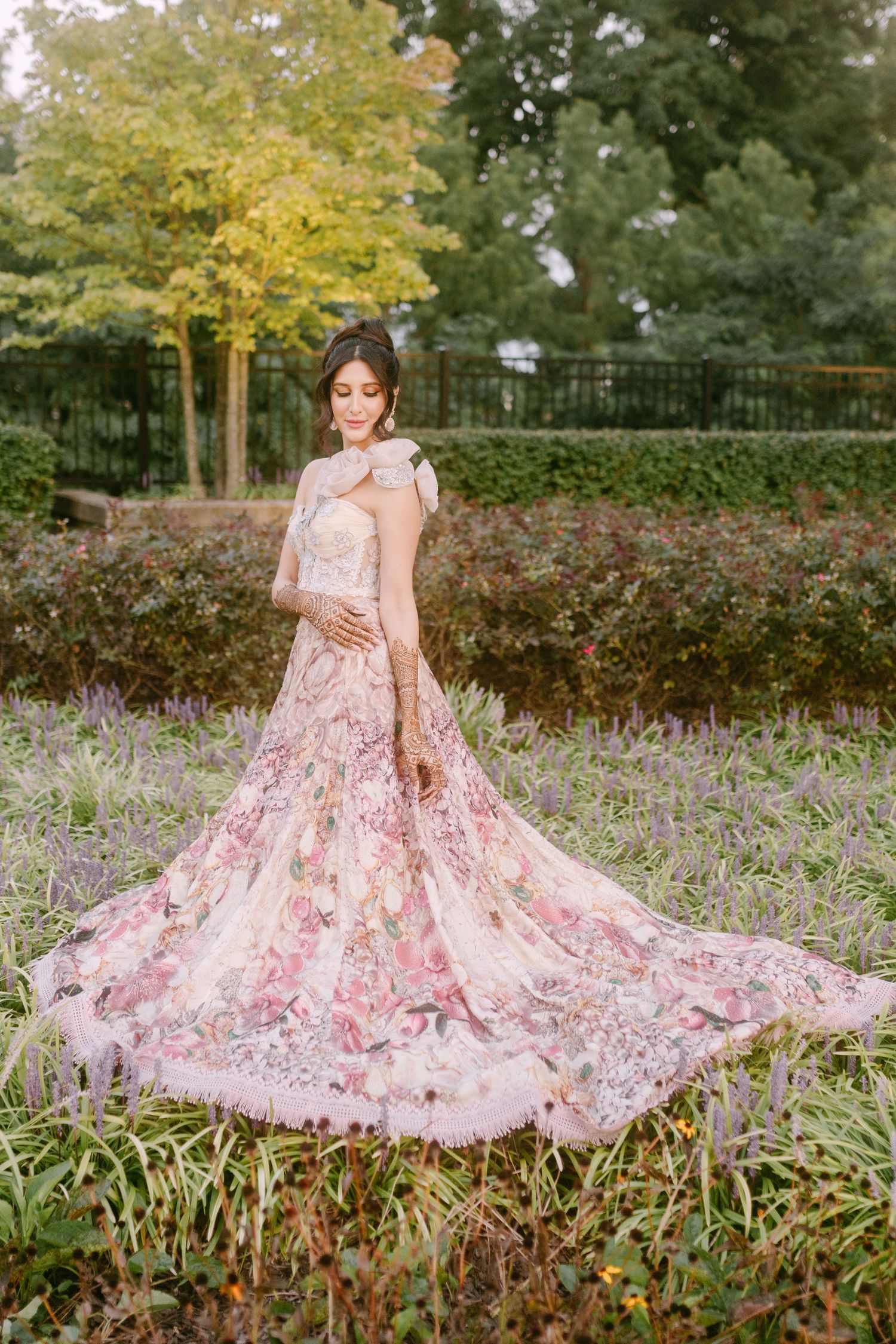 Floral embroidered pink reception gown photographed in a garden setting.