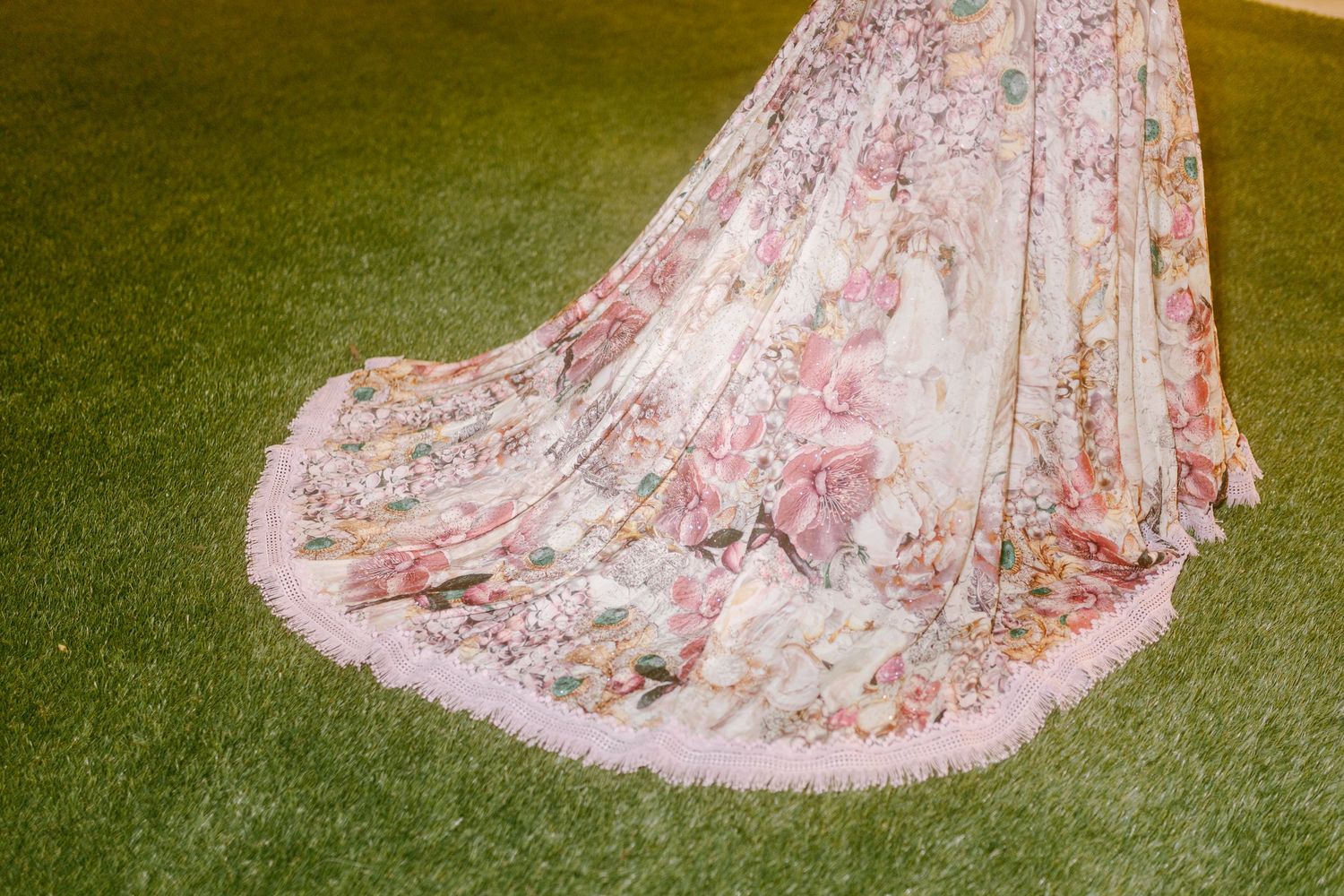 Close-up of a flowing dress train with delicate pink and white floral patterns on green grass.