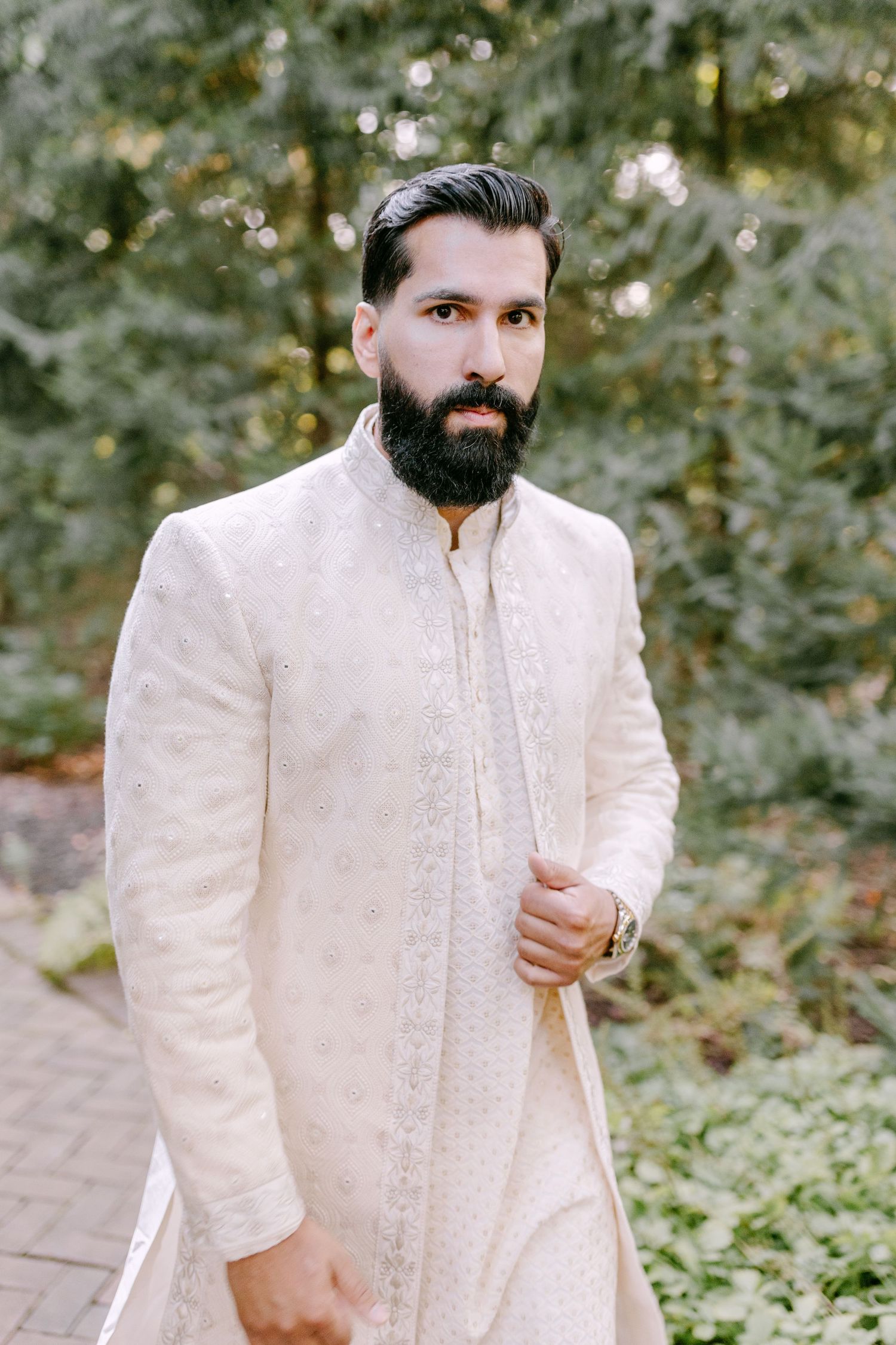 Elegant cream colored sherwani with detailed embroidery and mandarin collar in outdoor setting.