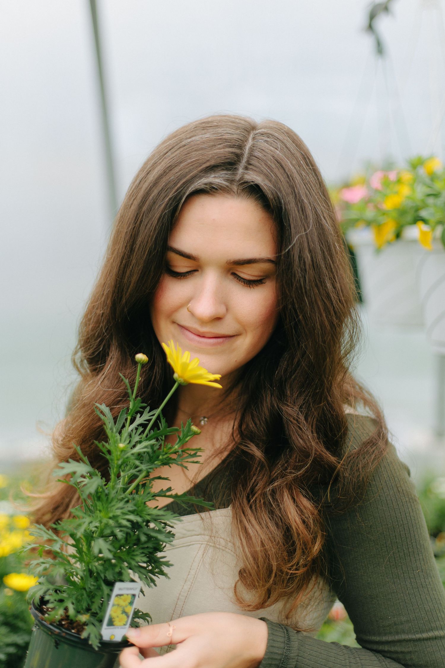 Woman holding yellow flowers while smiling in peaceful greenhouse environment.