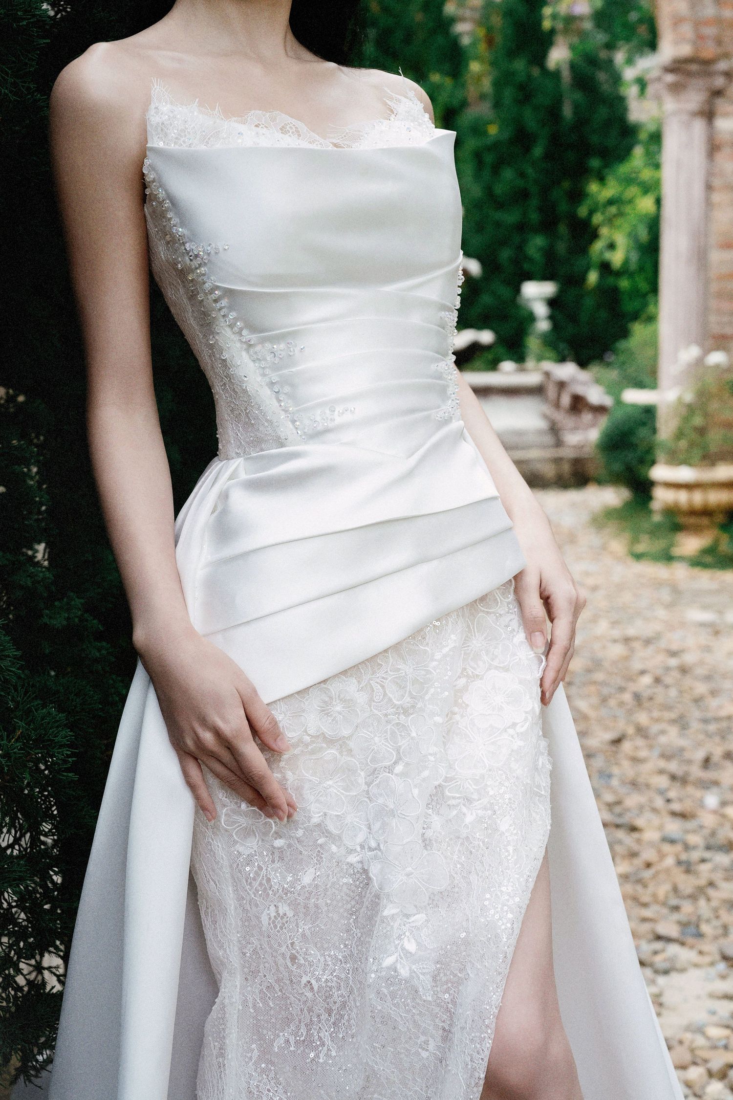 Elegant white bridal gown with asymmetrical draping and lace detailing features a sophisticated slit design.