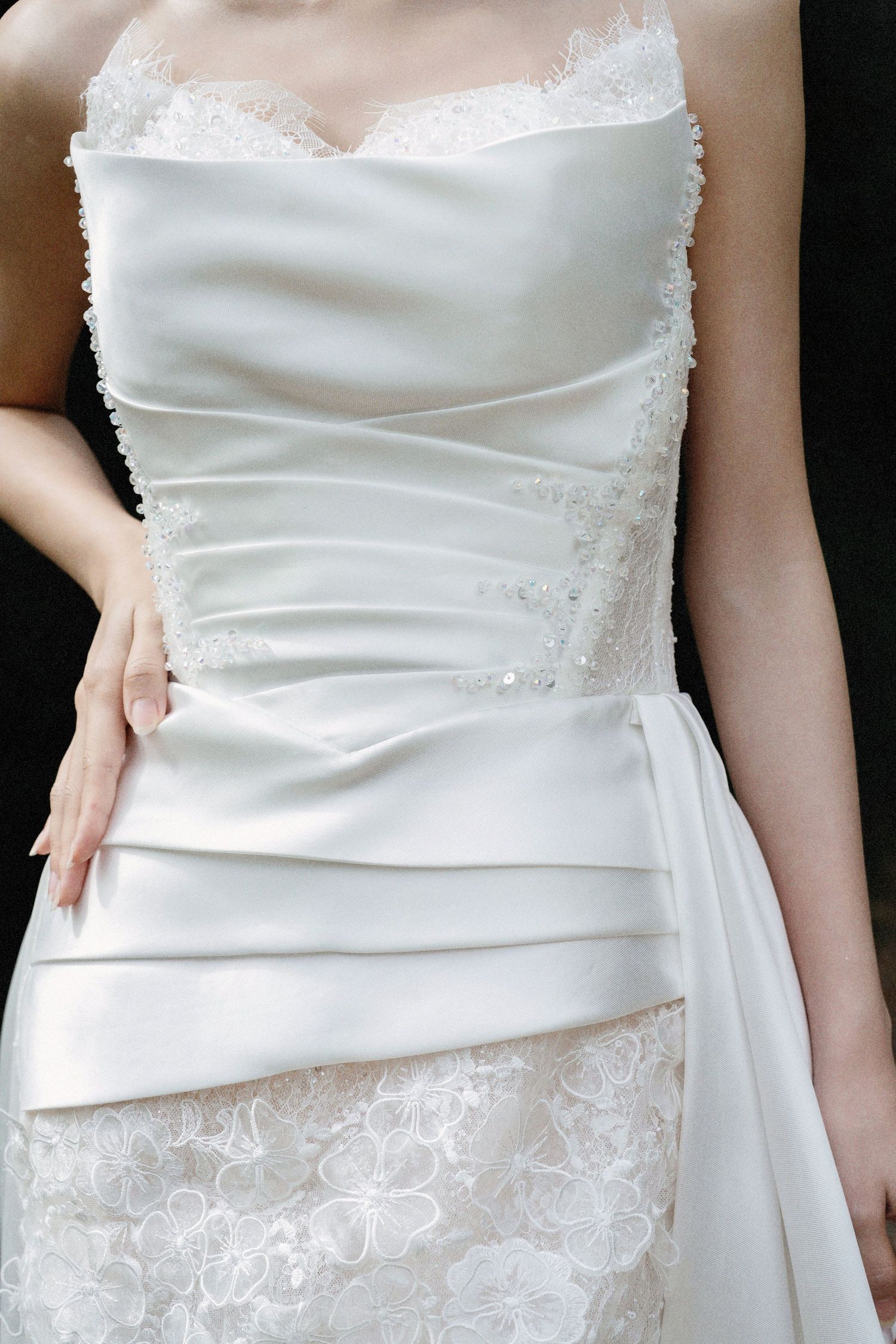 Elegant white wedding dress with ruched bodice details, delicate lace trim and asymmetrical draping on fitted silhouette.