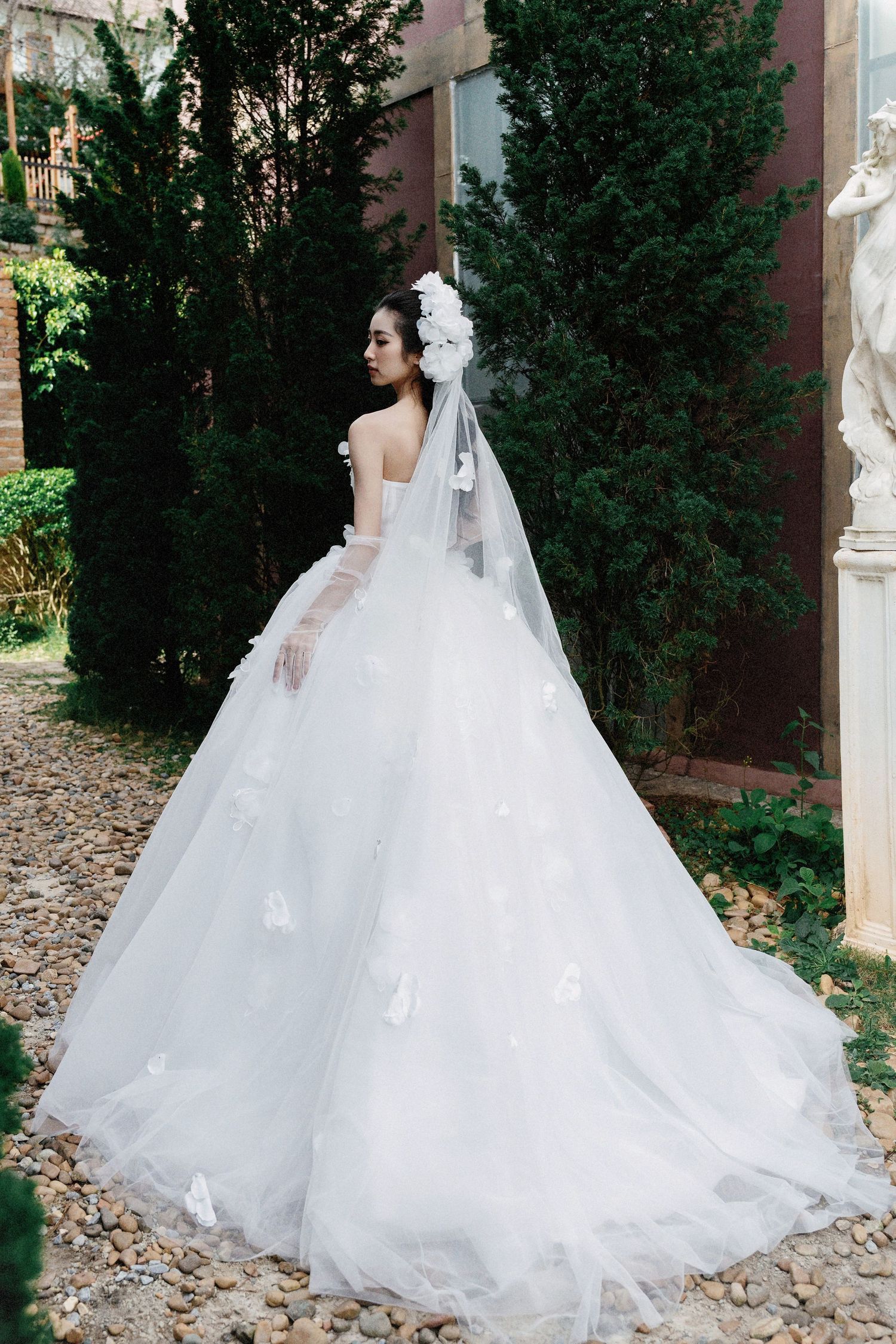 Beautiful white wedding gown with long cathedral train and veil photographed from behind in a garden setting.