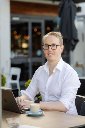 Professional in a white shirt works on laptop at outdoor cafe with coffee cup on wooden table.