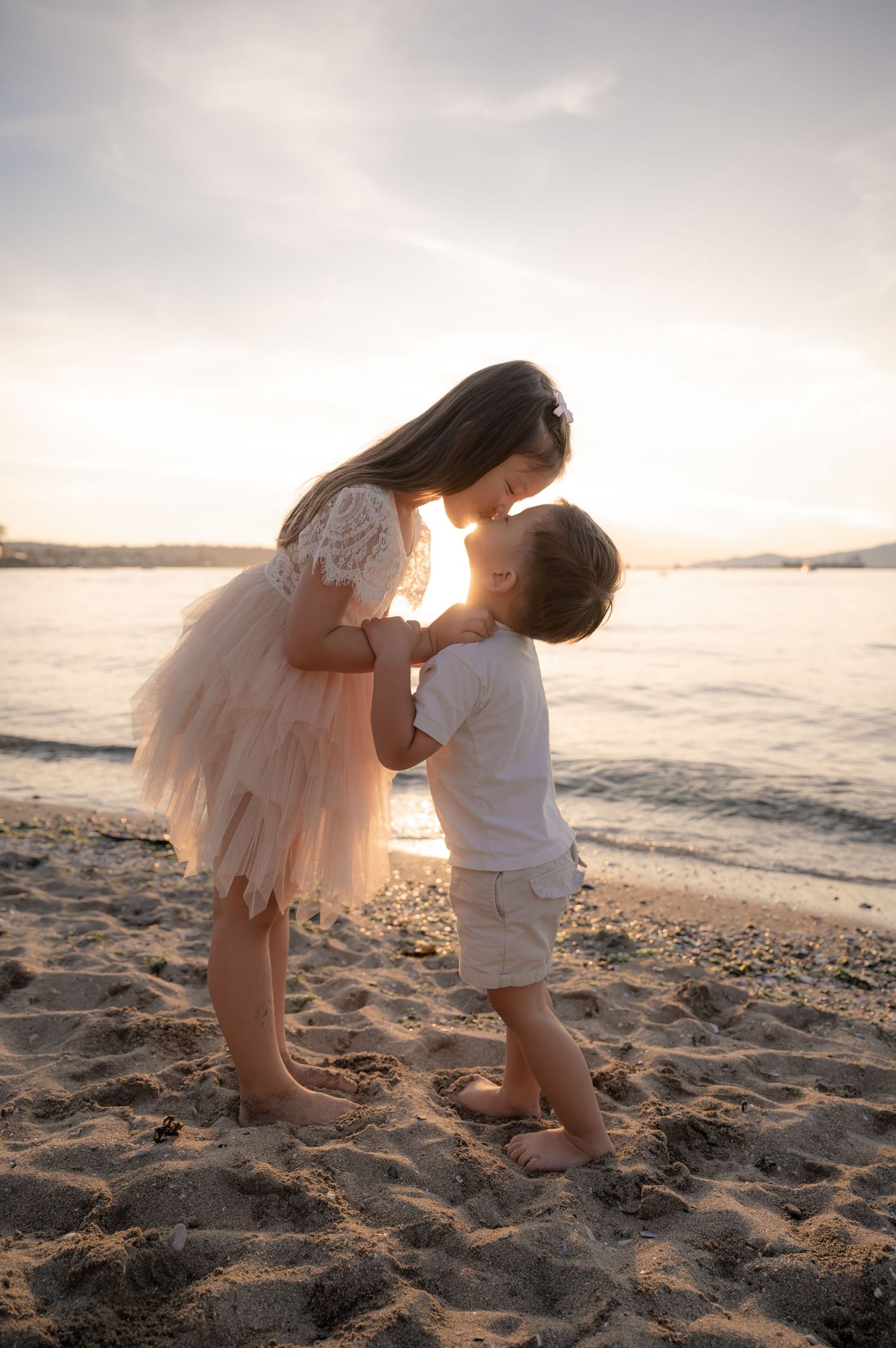 A tender moment captured at sunset on a beach, as two figures embrace on the sandy shore with golden light behind them.