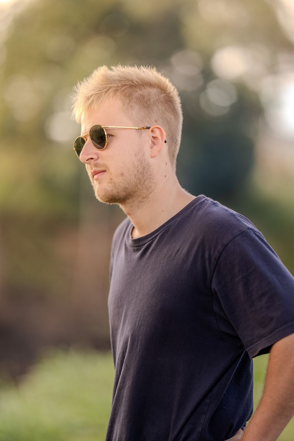 Side view of a person wearing a navy t-shirt and aviator sunglasses in golden afternoon sunlight.