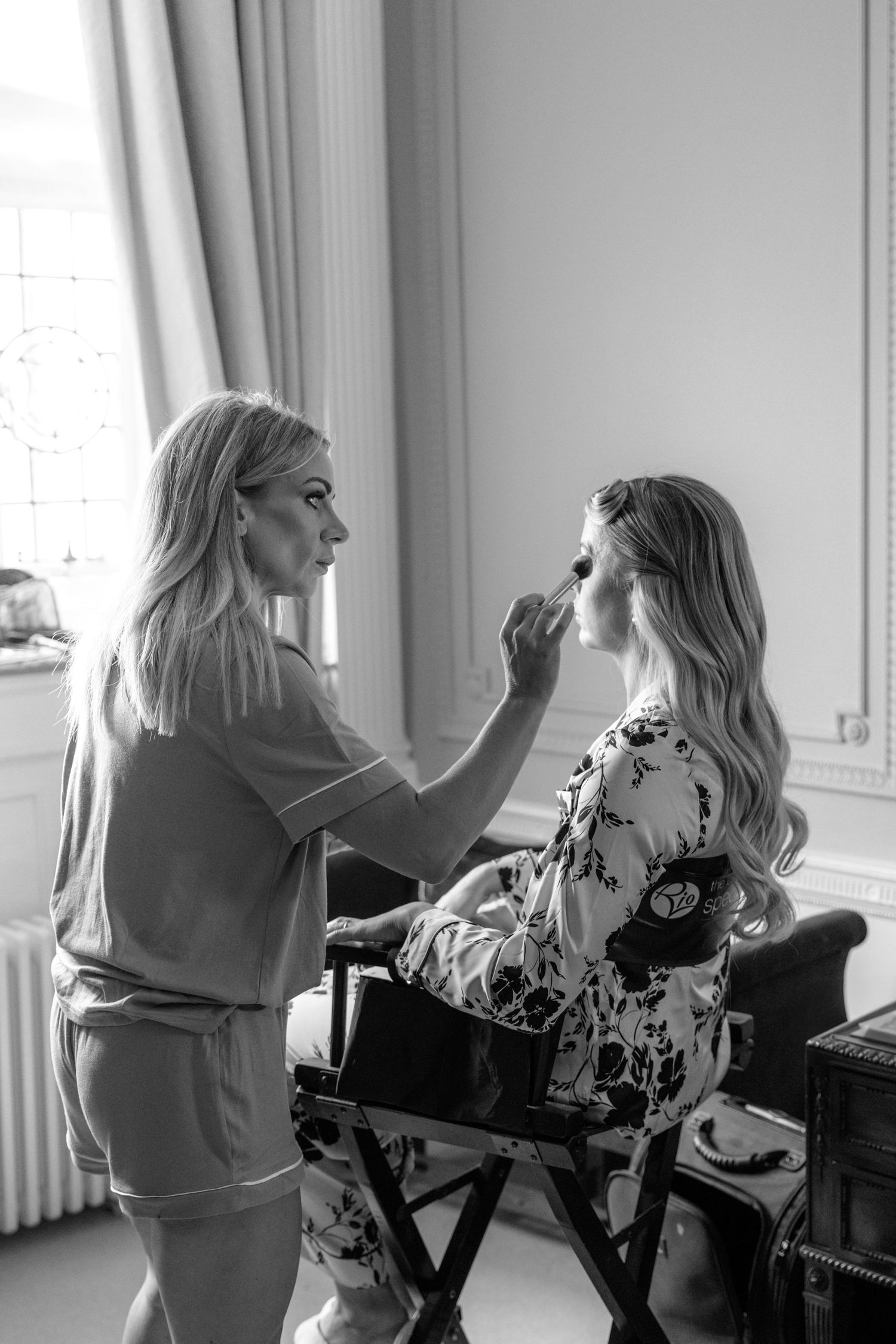 Makeup artist applying cosmetics to bridesmaid during wedding preparations.