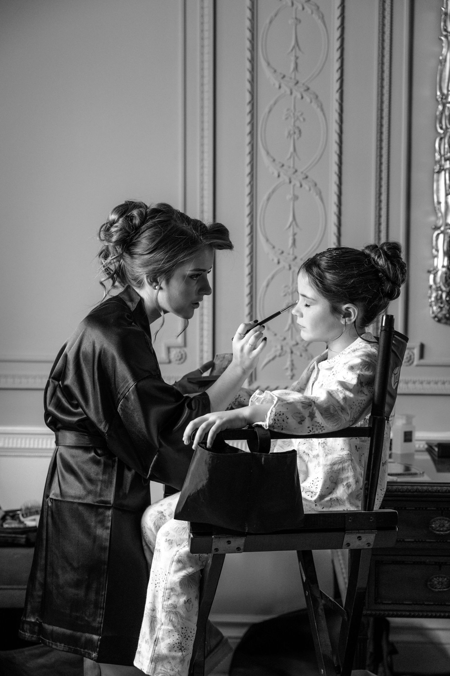 Makeup artist applying cosmetics in an elegant room with ornate wall moldings.