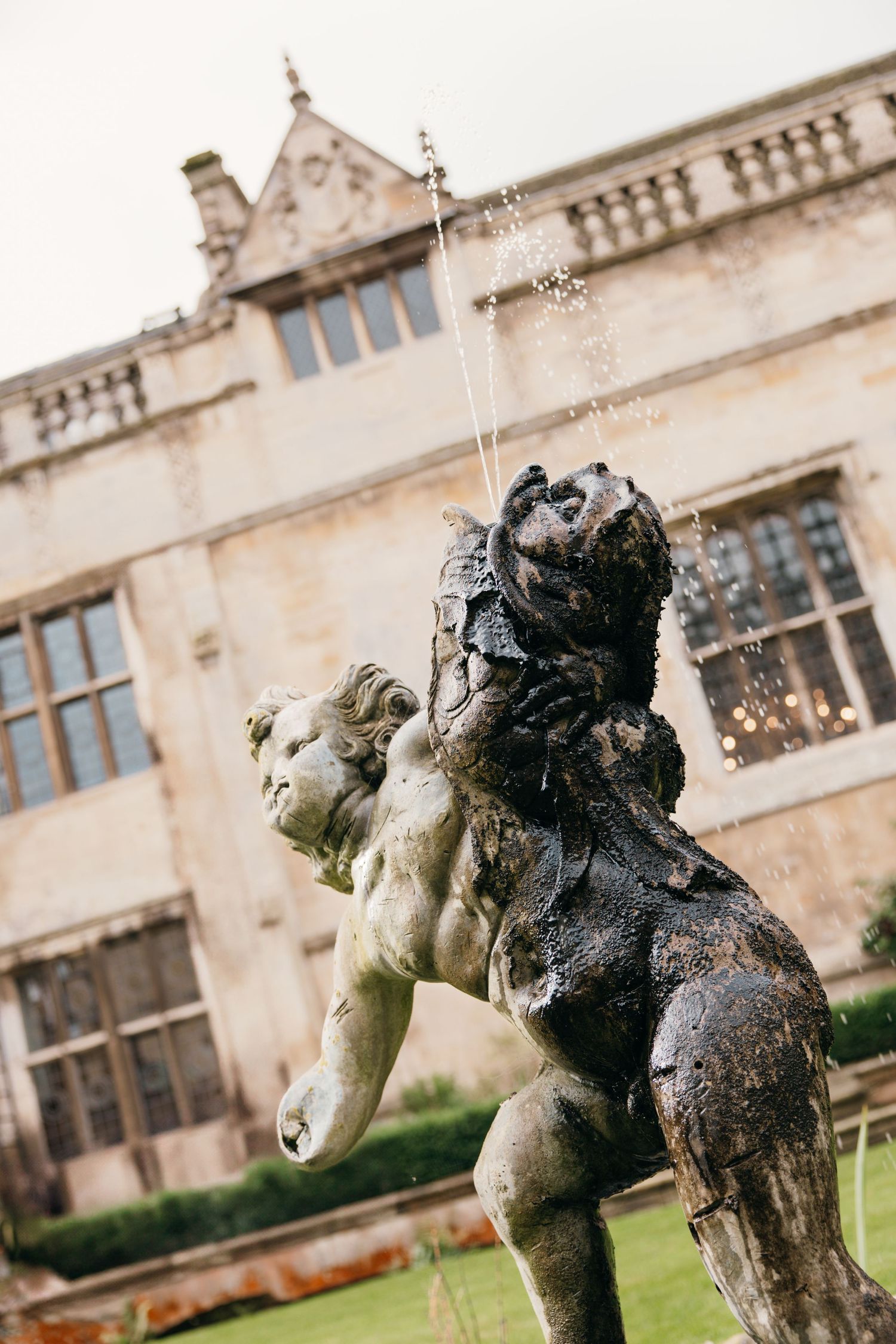 Stone fountain sculpture of two figures spraying water in front of a historic building facade.
