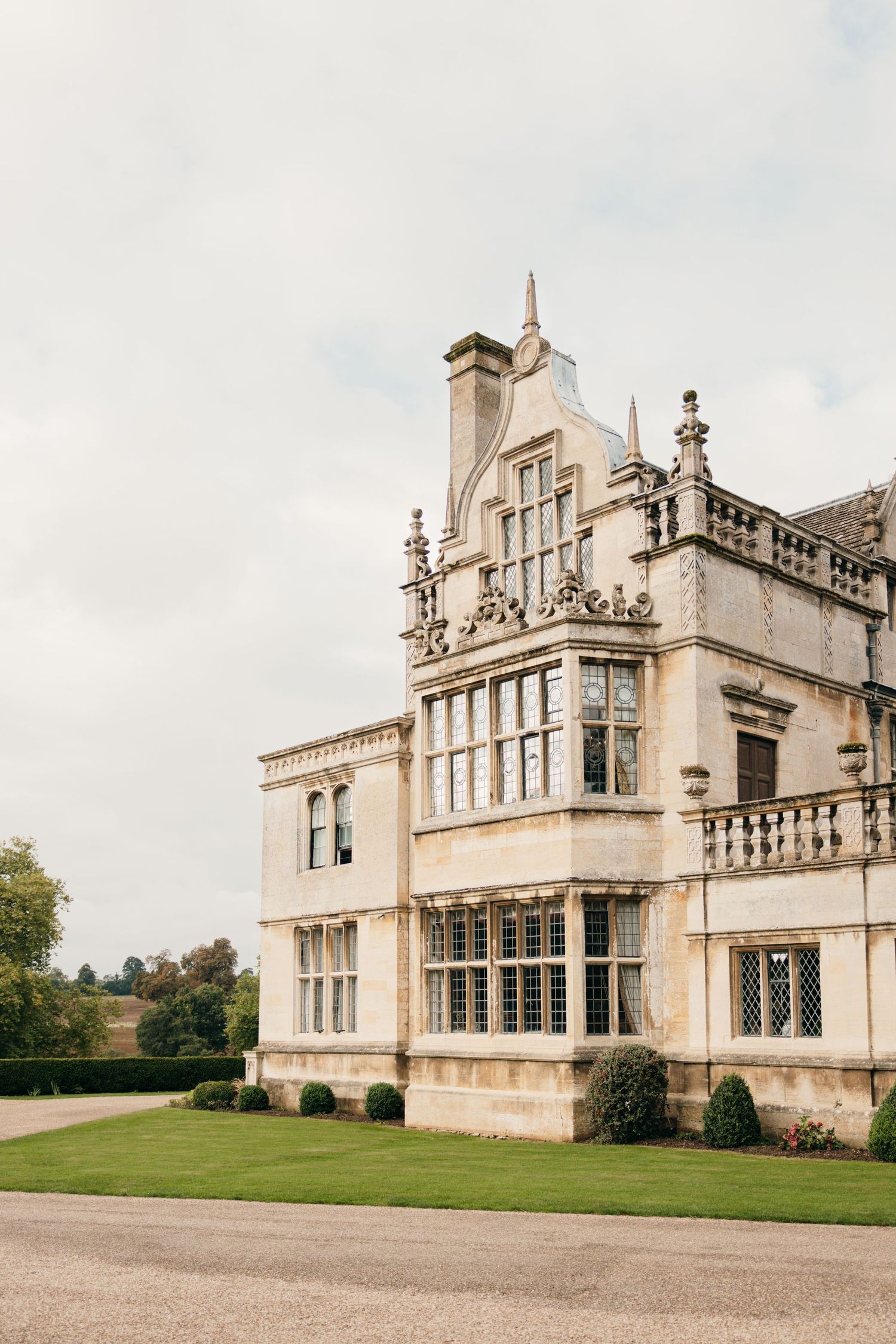 Elegant English manor house with Gothic architecture and ornate stone details against cloudy sky.