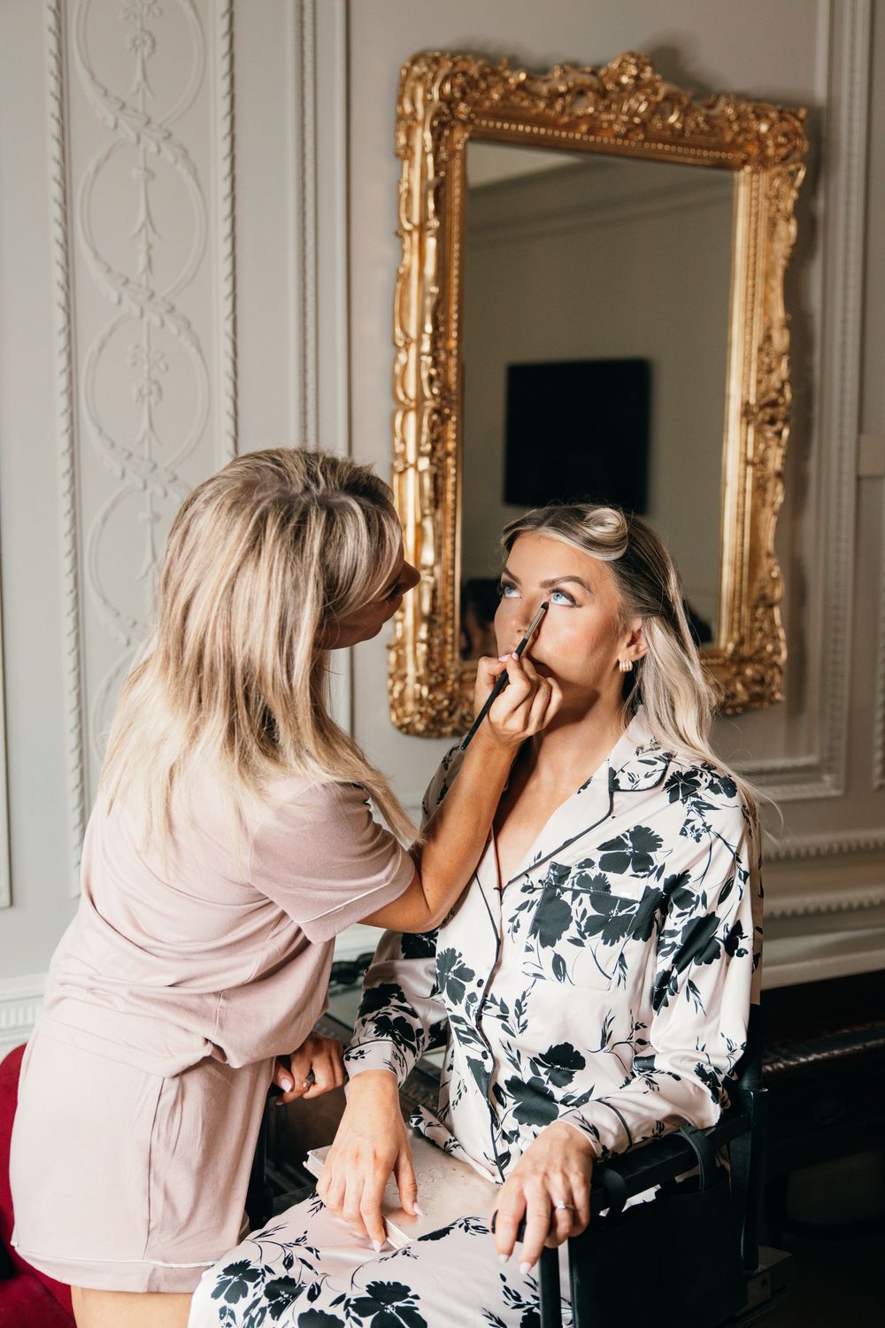 Wedding preparation scene with makeup application in front of ornate gold mirror.