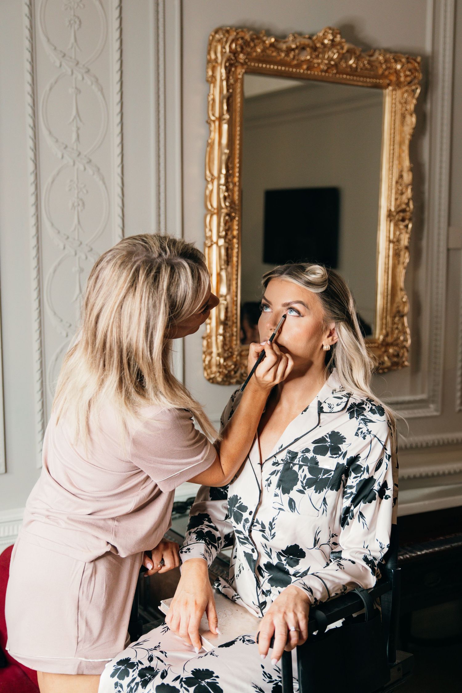 Wedding preparation scene with makeup application in front of ornate gold mirror.