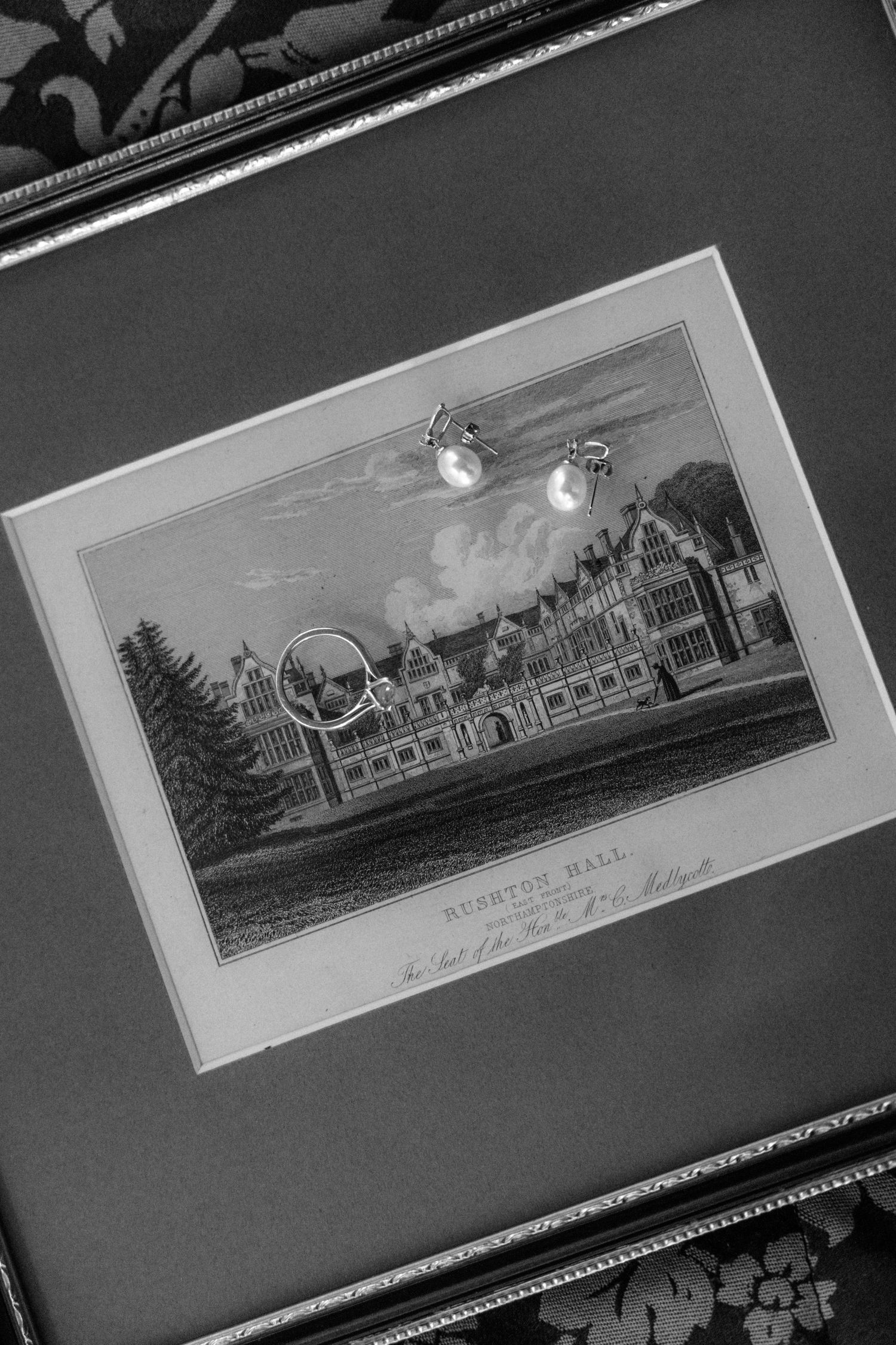 Black and white photograph of a vintage architectural drawing with pearl earrings displayed.